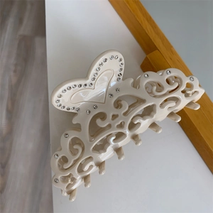 Detail view of cream-colored acetate shark hair claw with hollow hearts and rhinestones