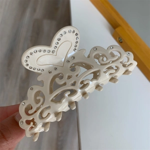 Detail shot of heart-shaped acetate claw clip with hollow vine pattern and rhinestones