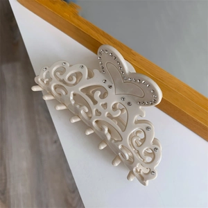 Detail view of cream acetate hair claw clip with hollow floral carving and rhinestones