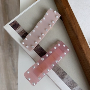 Détail de pinces à cheveux carrées en rose et crème ornées de perles blanches