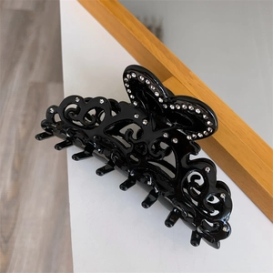 Detail view of vintage black hollow hair claw clip with floral carving and sparkling rhinestones