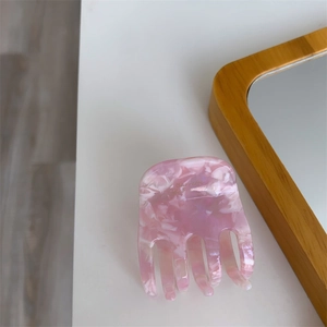 Detail of pink marble acetate hair claw clip with gold French lettering on white surface