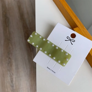 Détail d'une pince à cheveux vert clair avec perles sur carte de présentation blanche