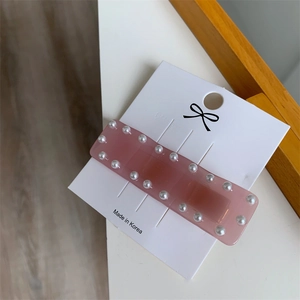 Détail d'une barrette en résine rose bordée de perles sur carte de présentation