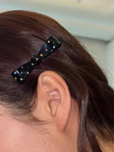 Detail view of a black bow hair clip with colorful rhinestones worn on hair side