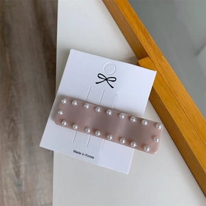 Gros plan d'une barrette rectangulaire en résine rose ornée de perles blanches