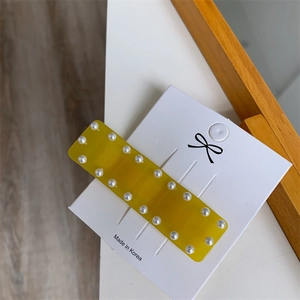 Détail d'une pince à cheveux rectangulaire jaune avec perles et résine translucide