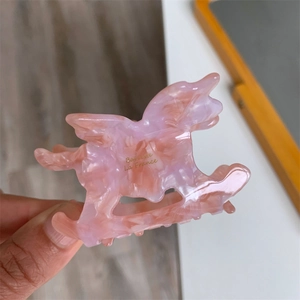 Détail de la pince à cheveux en acétate rose marbré en forme de cheval à bascule