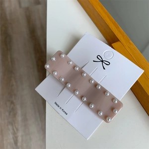 Détail de la barrette en acrylique rose avec deux rangées de perles sur support blanc