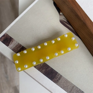 Détail d'une pince à cheveux en acétate jaune gingembre ornée de perles sur fond de magazine