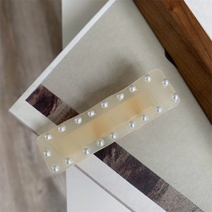 Détail d'une pince à cheveux rectangulaire en résine crème avec bordure en perles