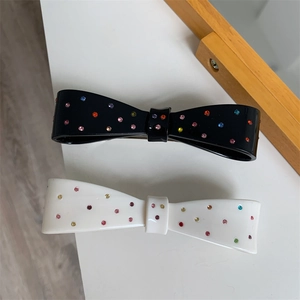 Detail view of black and white bow hair clips with colorful rhinestones on a white surface