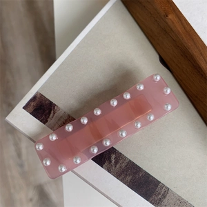 Détail d'une barrette rose en résine ornée de perles sur fond en bois chaleureux