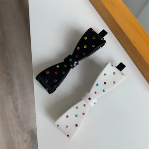 Detail of black and white bow hair clips with colorful rhinestones on a white surface