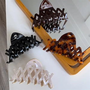 Dettaglio di tre mollette per capelli in acetato con trama geometrica su base bianca