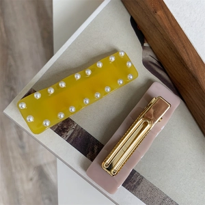 Détail d'une pince à cheveux jaune à perles et d'un clip bec de canard rose pour femme