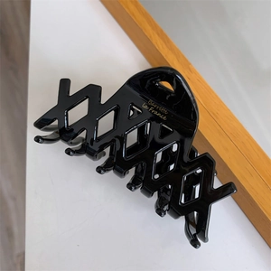 Dettaglio molletta capelli nera in acetato con griglia geometrica e scritte dorate