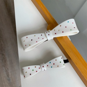Detailed macro view of white bow hair clips with colorful rhinestones on a wooden frame