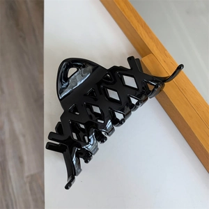 Dettaglio di una grande molletta per capelli nera in acetato con design geometrico vuoto