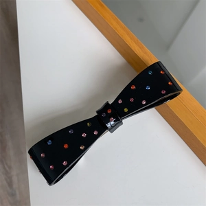 Close-up of black bow hair clip with colorful rhinestones on polished resin finish