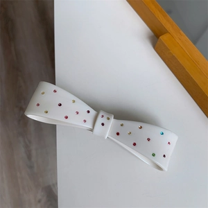 Detail of white resin bow hair clip with colorful rhinestones on a white surface