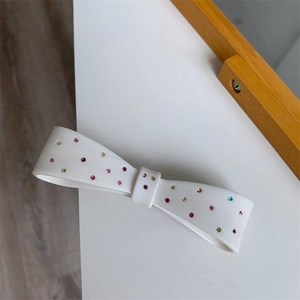 Detailed view of white resin bow hair clip embellished with colorful sparkling rhinestones