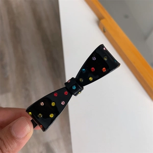 Detailed view of black bow hair clip with colorful rhinestones on a hand