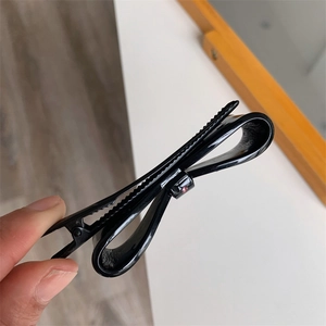 Close-up of black acetate bow hair clip with a pink rhinestone detail on a duckbill base