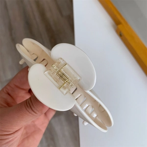 Detail of a creamy white acetate hair claw clip showing durable gold spring and teeth