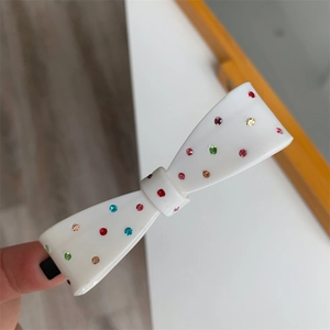 Detail of white acetate bow hair clip with colorful rhinestones held by hand