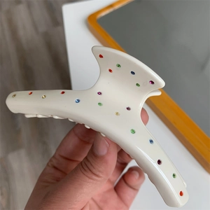 Détail d'une pince à cheveux crème avec des strass colorés tenue par une main