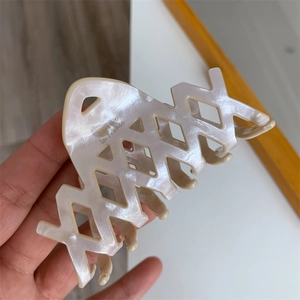 Dettaglio della grande molletta per capelli in acetato con texture marmorizzata e design a X