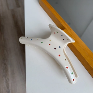 Détail d'une pince à cheveux crème ornée de strass multicolores sur une surface blanche