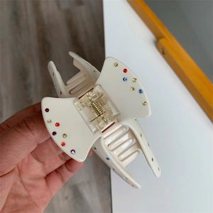 Détail d'une pince à cheveux en acétate blanc crème avec strass colorés et ressort en métal