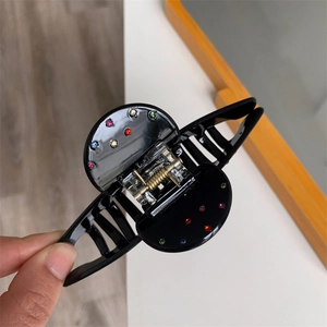 Vue détaillée de la grande pince à cheveux noire avec strass colorés et ressort doré