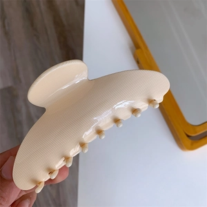 Detailed view of large beige acetate claw clip with vertical striped texture held in hand