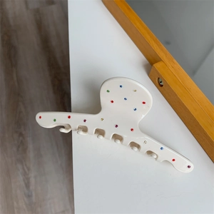 Détail de la pince à cheveux crème ornée de strass colorés sur une surface blanche