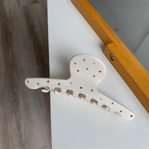 Détail d'une pince à cheveux crème ornée de strass colorés sur une surface blanche