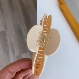 Detail of cream hair claw clip showing durable gold metal spring and sturdy teeth grip