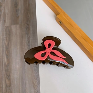 Gros plan d'une pince à cheveux en acétate marron chocolat avec détail de nœud rose poli