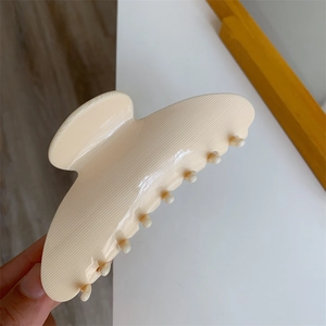 Detail shot of a large cream acetate hair claw clip featuring horizontal textured patterns