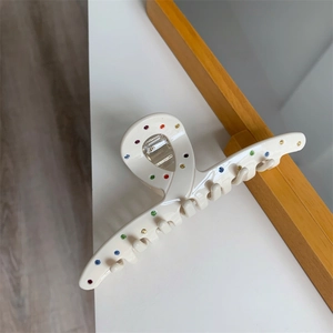 Détail d'une pince à cheveux blanc crème ornée de strass colorés sur une table