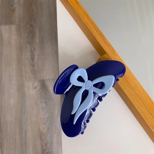 Détail d'une pince à cheveux en acétate bleu foncé avec un nœud bleu sur un bureau