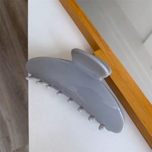 Detail view of large grey acetate hair claw clip with glossy finish on a minimalist desk