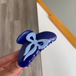 Détail d'une pince à cheveux en acétate bleu foncé avec nœud bleu clair tenue en main