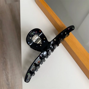 Détail de la pince à cheveux noire avec strass colorés sur une surface blanche