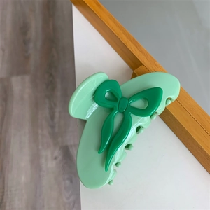Gros plan d'une pince à cheveux vert clair avec nœud vert foncé sur surface blanche