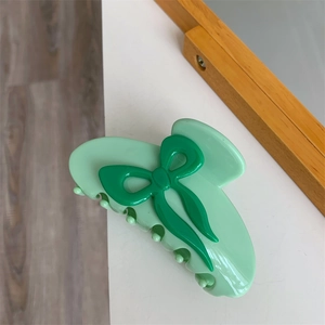 Détail de la pince à cheveux en acétate vert avec un motif de nœud papillon 3D