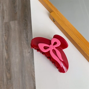 Détail d'une pince à cheveux en acétate rouge foncé avec un nœud rose sur fond blanc