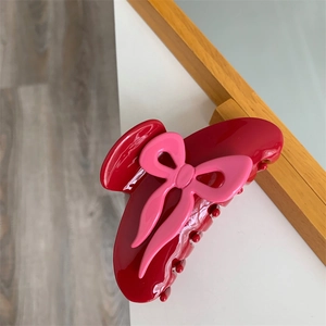 Détail d'une pince à cheveux bordeaux en acétate avec un nœud rose 3D sur bois